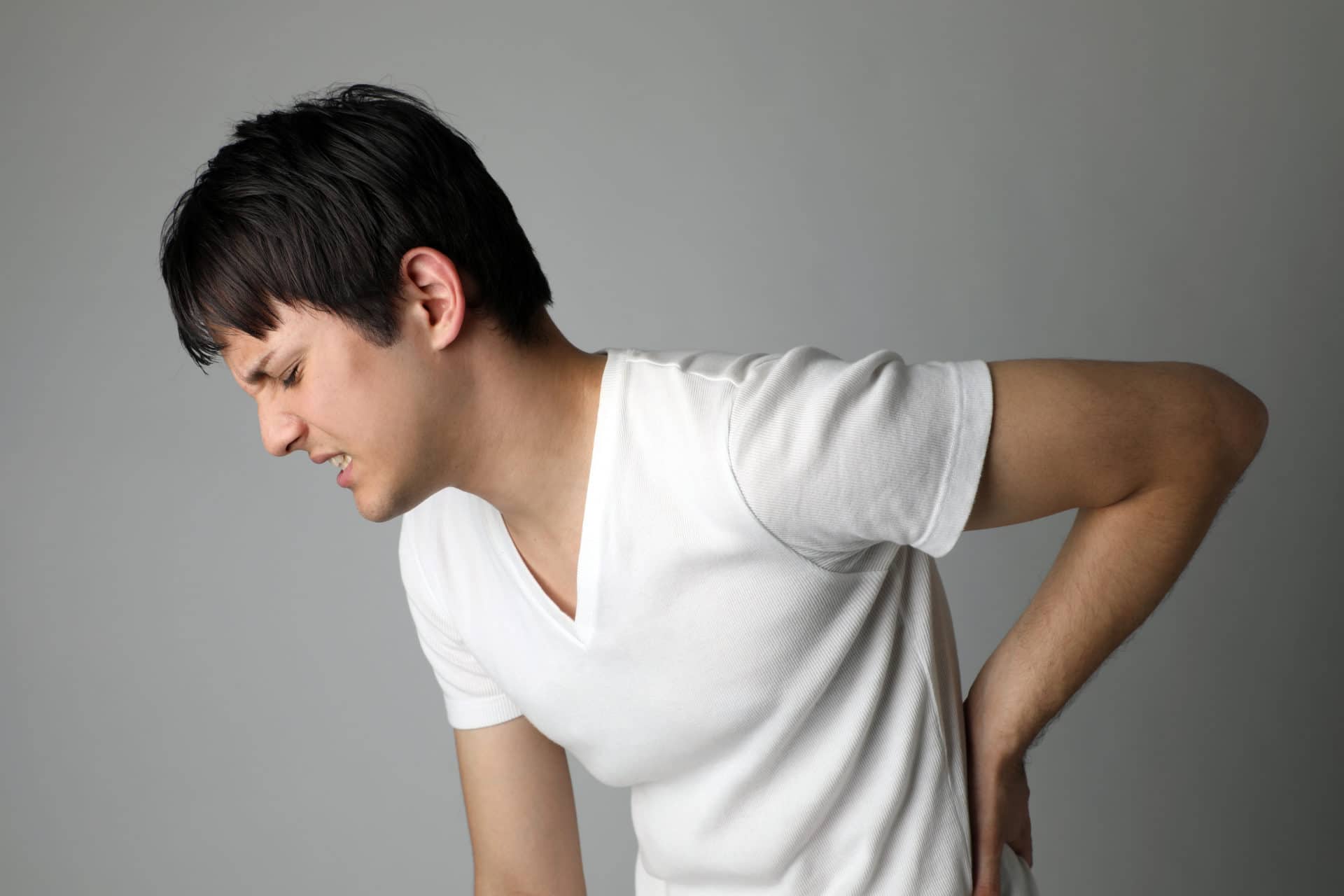 side profile of man in white t-shirt hunched over with back pain